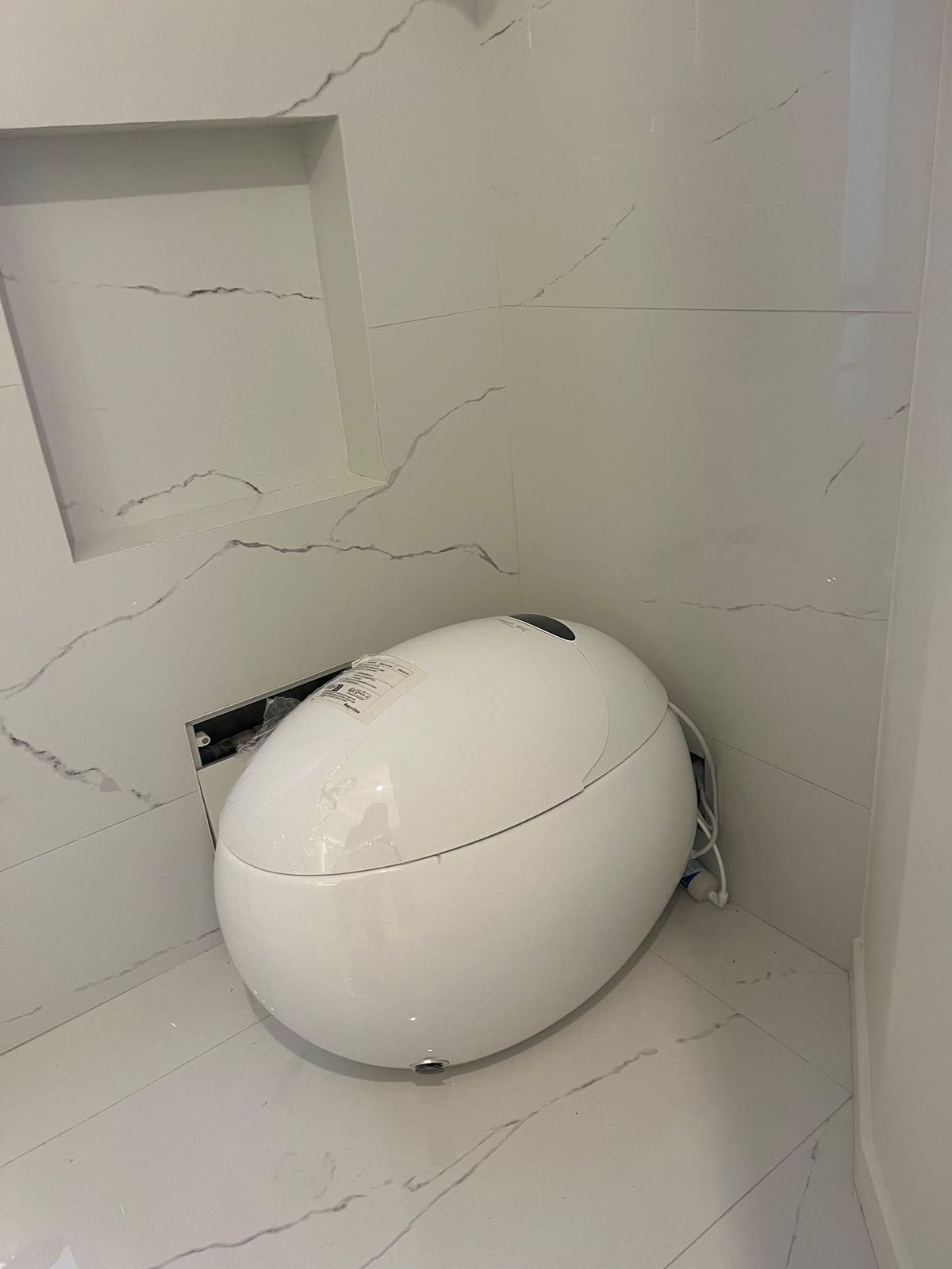 WC japonais blanc au sol installé chez un client dans une pièce au carrelage effet marbre.