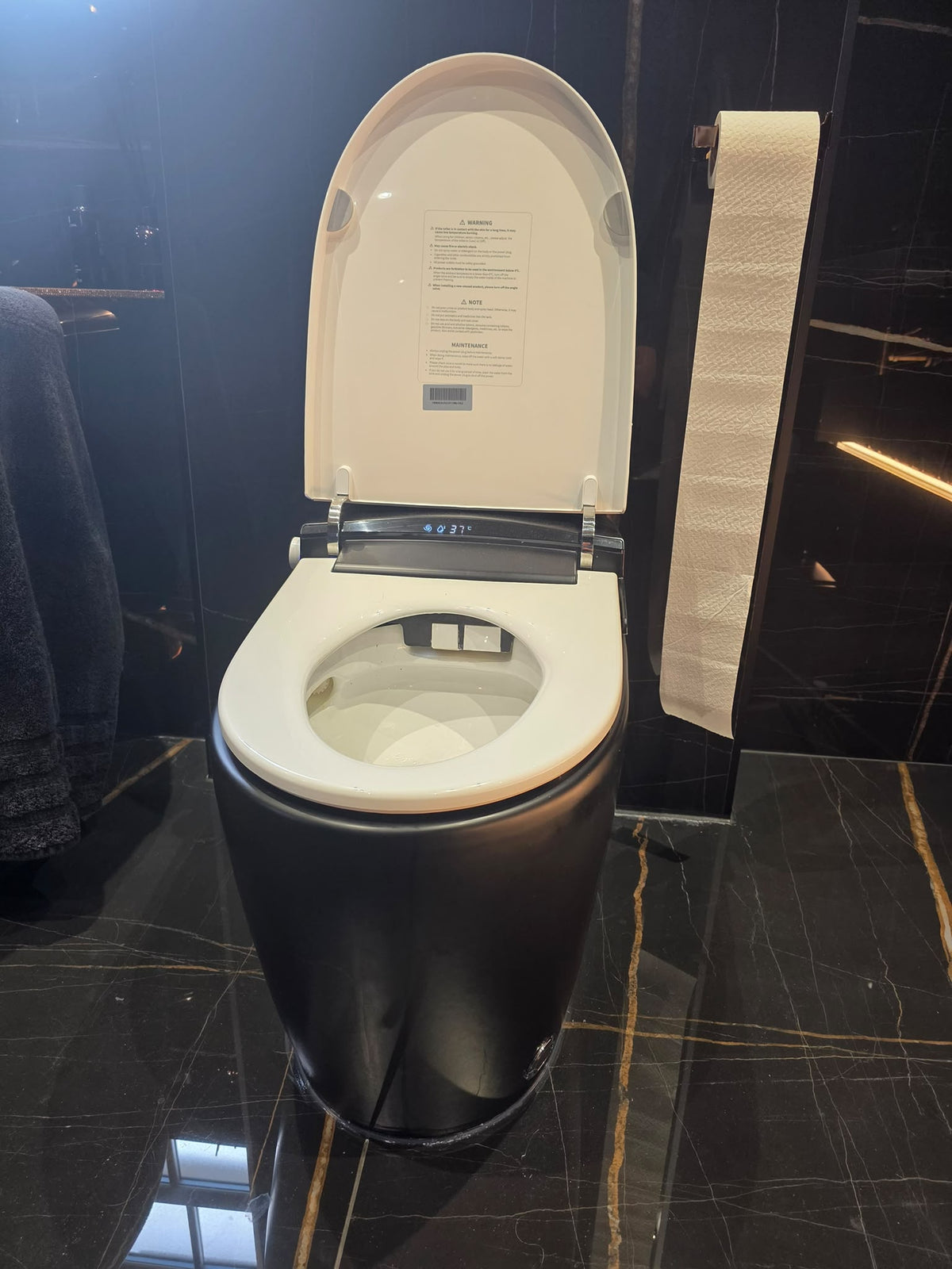 WC japonais noir avec abattant blanc ouvert installé chez un client dans une pièce au carrelage noir veiné d’or.