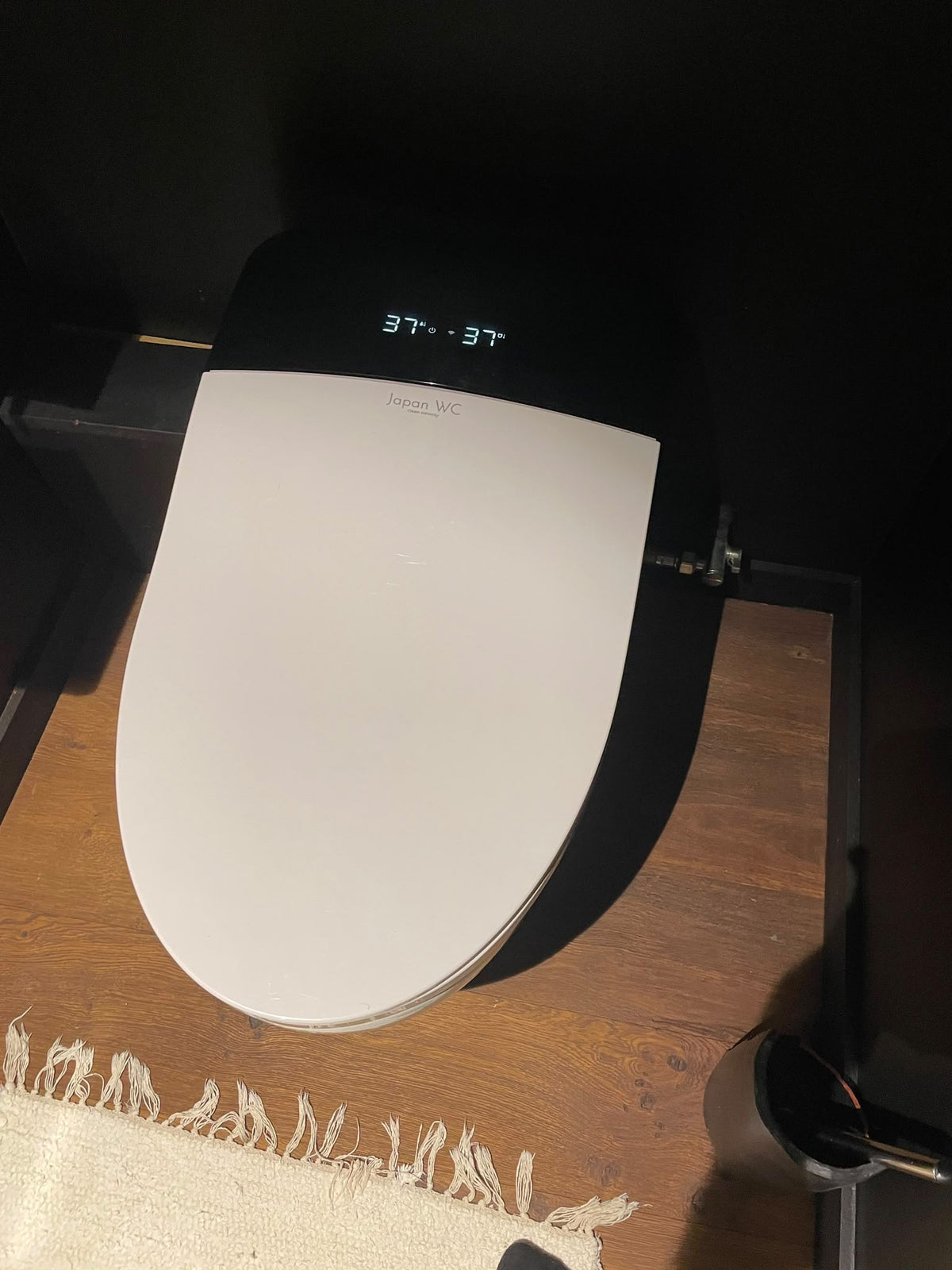 WC japonais noir avec abattant blanc installé chez un client, sur un sol en bois.
